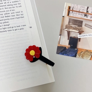 Detail view of red and yellow daisy hair clip on an open book for aesthetic display