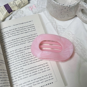 Pink pearlescent marble hair claw clip for women displayed on vintage book and lace