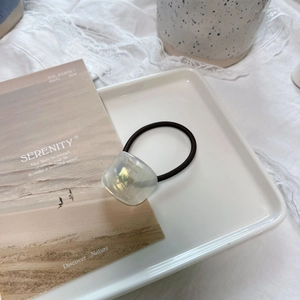 Macro detail of chic iridescent square charm with golden handmade text on black hair tie