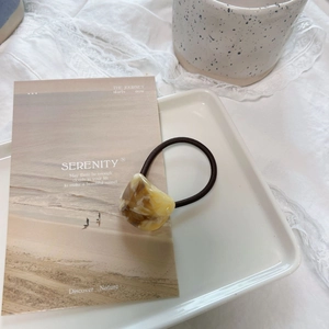 Close-up of elegant acetate hair tie with marble texture on ceramic tray background