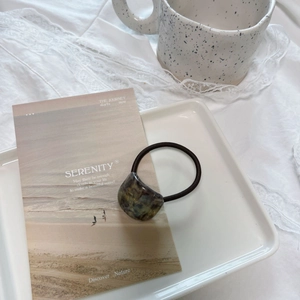 Close-up of hair tie with tortoiseshell resin charm on a minimalist ceramic tray