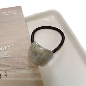 Minimalist marble-textured acetate hair tie with golden handmade lettering on a white tray