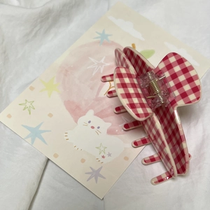 Detail view of red gingham acrylic shark hair clip with transparent spring on white fabric