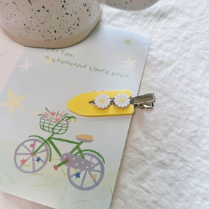 Detail view of yellow daisy duckbill hair clip with resin flowers on a decorative card