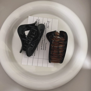 Top view of classic black and amber hair claws in a white tray with aesthetic card