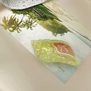 Pale green shell hair claw with floral patterns and pink bow on a beach postcard background