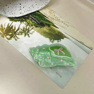 Detail of a light green conch-shaped hair claw clip with pink floral and bow decorations