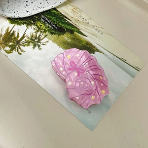 Detail of pink conch hair claw with bow and star patterns on a beach postcard background