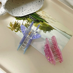 Detail view of two translucent butterfly hair claws in purple and pink with gold metal springs