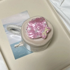 Pince à cheveux rose en forme de coquillage avec petit nœud jaune sur céramique