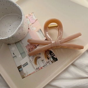 Macro shot of elegant nude pink bow hair claw clip with gold spring on a tray