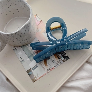 Detailed top view of a dark blue bow-shaped hair claw clip on a stylish beige tray