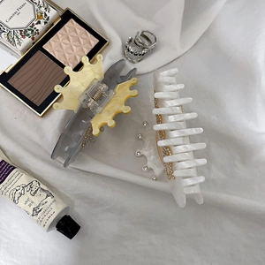 Detail of crown acrylic hair claw clips with rhinestones on a white fabric background
