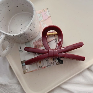 Detail of dark red bow hair claw clip with golden spring on a ceramic tray