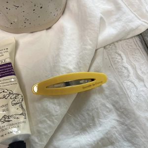 Detail of yellow oval barrette hair clip with gold label on soft white fabric background