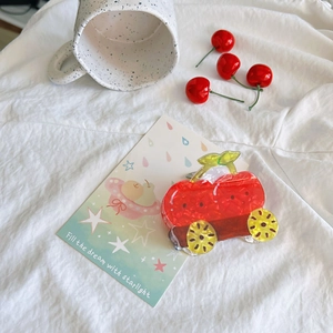 Close-up of red car-shaped hair claw clip with black dots on a white fabric surface