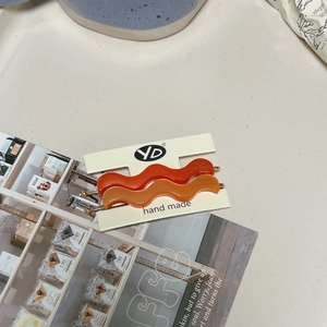 Detail of wavy acetate hair clips in orange and amber on a handmade display card