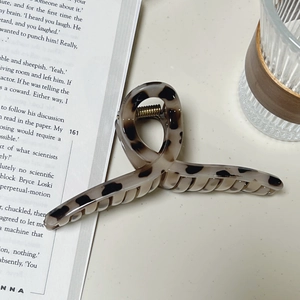 Grande pince à cheveux léopard écaille de tortue posée sur un livre près d'un verre