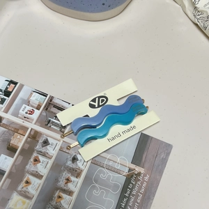 Detail view of wavy acetate hair clips in Morandi blue and teal with gold label