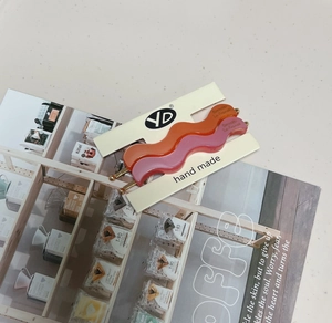 Detail showing two wavy matte hair clips in pink and orange on a brand display card