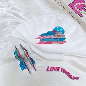 Detailed macro view of two colorful butterfly acrylic hair claws on a decorative shell plate