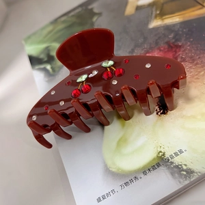 Retro deep red acetate hair claw clip with crystal cherry decoration on a magazine