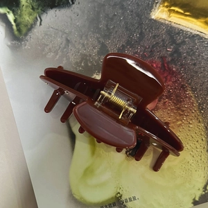 Close-up of a large burgundy acetate hair claw with a glossy finish and golden metal spring