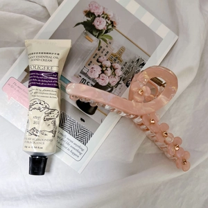 Elegante pinza para el pelo con flor rosa pálido y cuentas doradas sobre fondo de tela blanca
