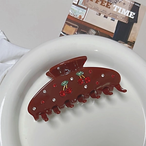 Detailed view of dark brown cherry hair claw clip with red rhinestones on a ceramic plate