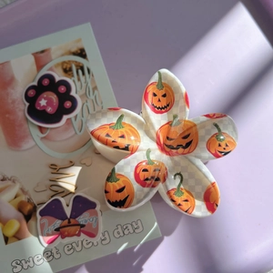 Detailed view of cream flower hair claw clip with orange Halloween pumpkin patterns