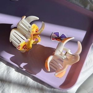 Close-up of two cream pizza print hair claws with 'BOO' text on a purple tray