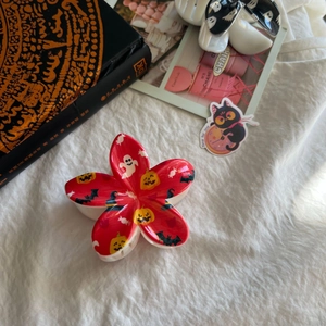 Détail d'une pince à cheveux rouge en forme de fleur avec motifs de citrouille et de fantôme