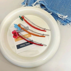 Barrettes à cheveux à fleurs en acétate rouge et orange sur une assiette blanche