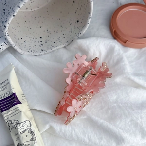 Pince à cheveux fleur rose en acrylique avec strass posée sur un tissu blanc texturé
