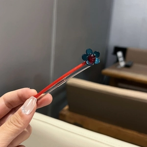 Détail d'une barrette à cheveux rouge avec une fleur bleue et une perle