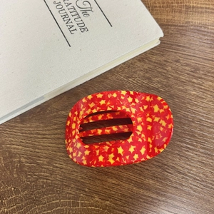 Red acetate star hair claw clip for high ponytail styling on a vintage book background