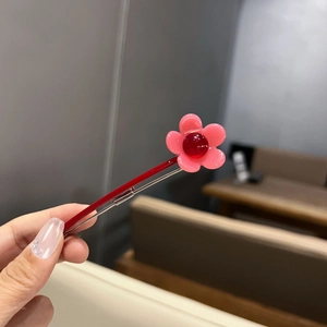 Détail d'une pince à cheveux fleur rose avec perle rouge et base en métal rouge