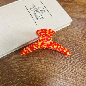 Macro detail of red and yellow floral star-shaped hair claw clip on wooden surface