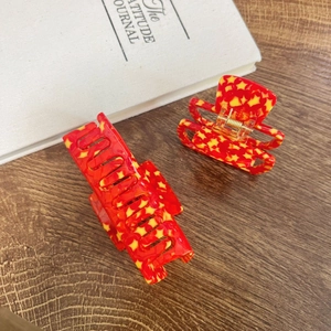 Detail of two red star-patterned hair claws showing sturdy gold springs and resin texture