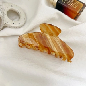 Detail showing amber textured hair claw clip with golden glitter on white fabric