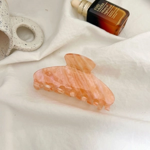 Detailed view of the large orange marble hair claw with gold glitter on white fabric