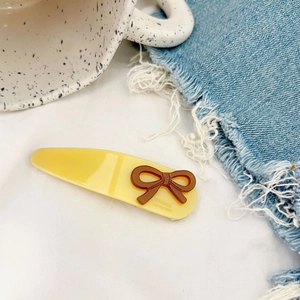 Detailed macro view of yellow acetate hair clip with brown bow and gold letter branding