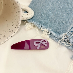 Detail of a purple water drop hair clip with a lilac bow and gold handmade logo