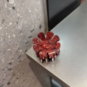 Dettaglio del fermaglio per capelli a fiore in acetato con trama marmorizzata rosso-marrone