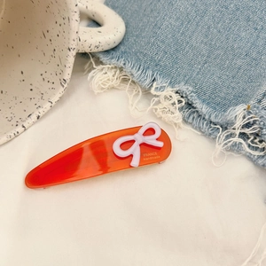 Close-up of translucent orange hair clip with 3D white bow and gold lettering detail