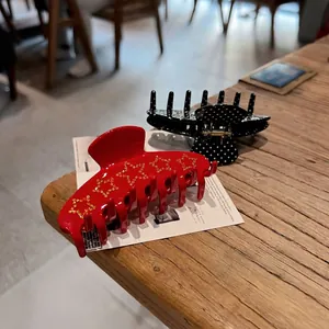 Star pattern red and polka dot black hair claws made of glossy resin on wooden table