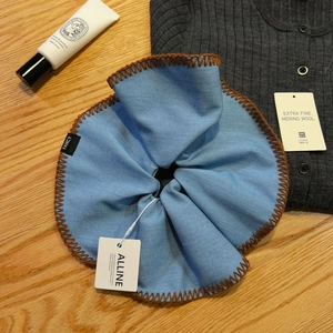 Elegant light blue scrunchie with brown stitched edges and woven label on a grey sweater
