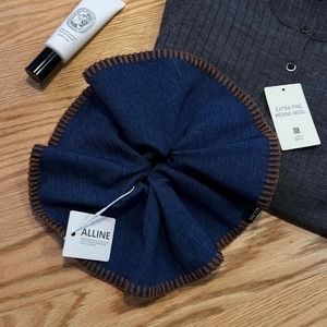 Detail of navy denim scrunchie with brown stitching and branding on wood surface