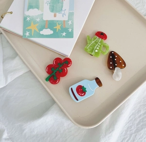 Detailed view of colorful acetate hair clips in tomato and mushroom shapes on a tray