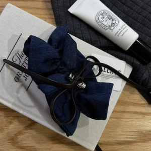 Close-up of a blue denim scrunchie with a brown leather bow and silver metal tips on a book